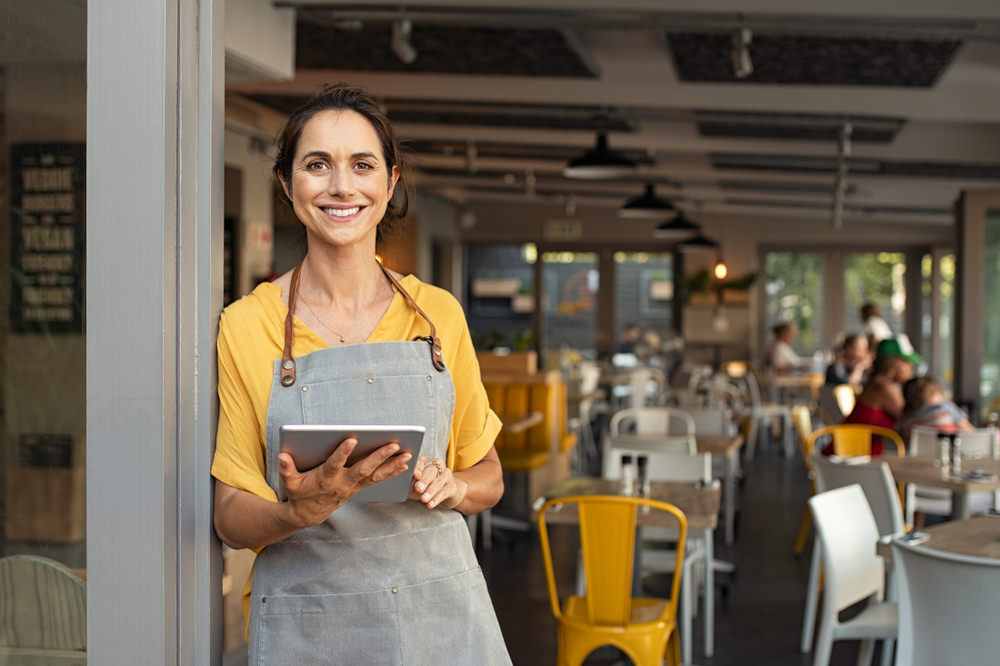 Portrait,Of,Happy,Woman,Standing,At,Doorway,Of,Her,Store. Reasonable Income for Age and Occupation